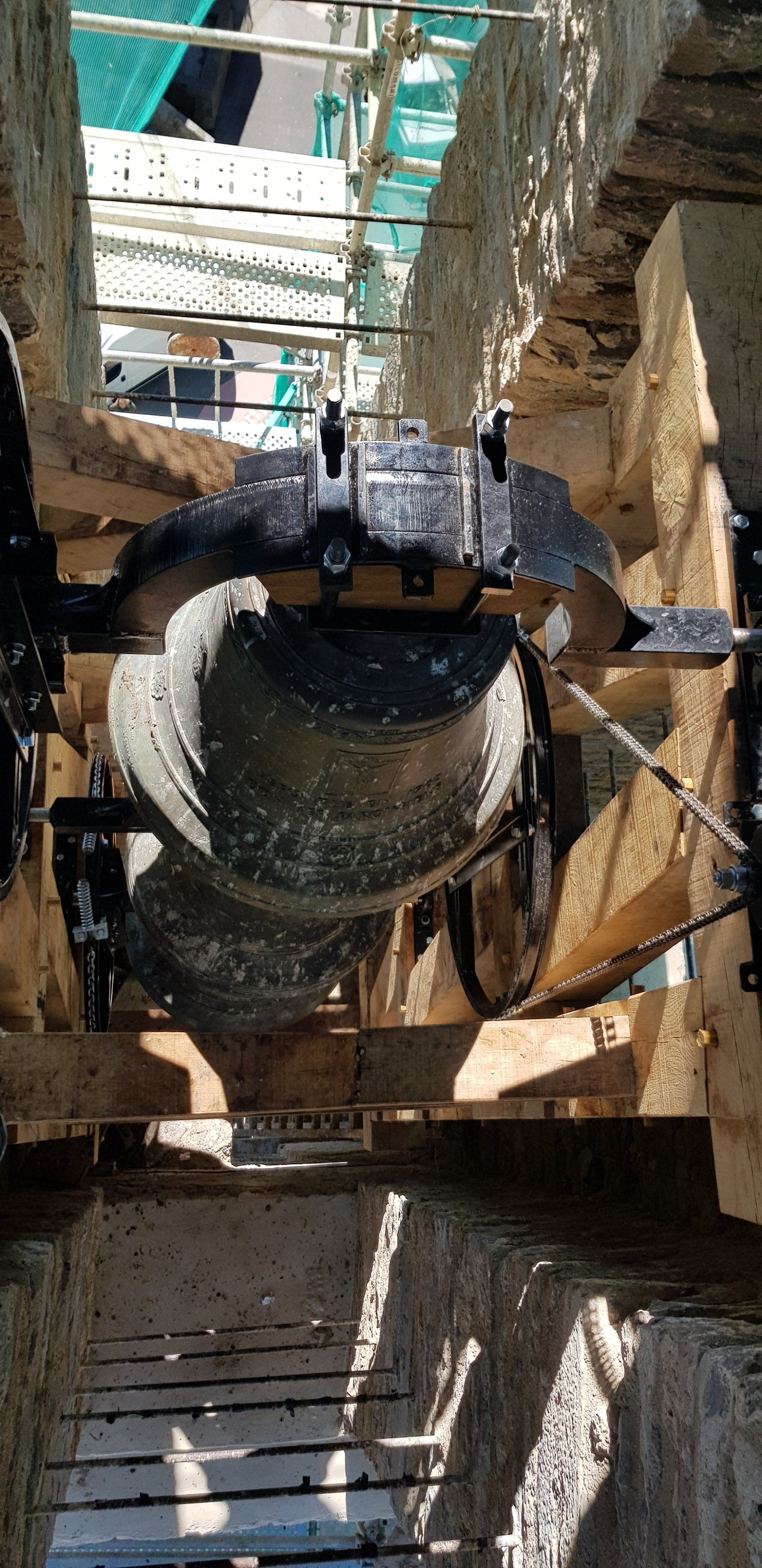 Cloche en bronze reposée sur son joug métallique sous échafaudage, dans un clocher en pierre